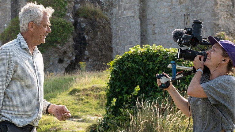 Two people filming the archaeological dig at Corfe Castle, Dorset with the castle ruins in the background